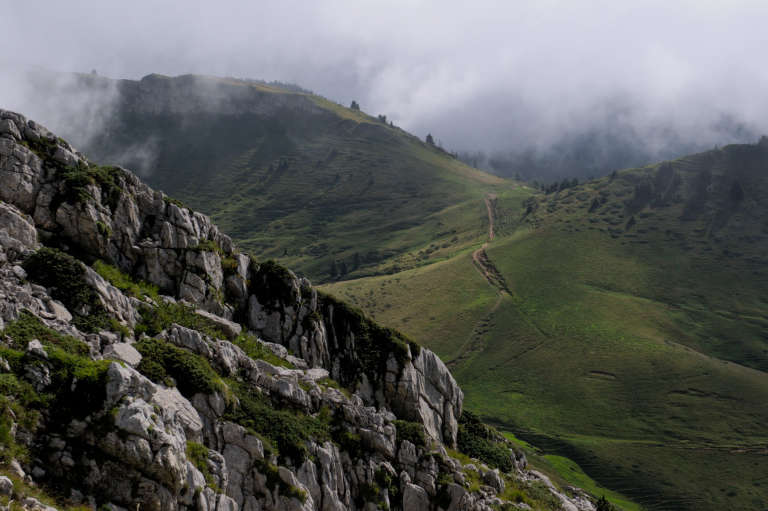 Paysage de moyenne montagne en Chartreuse avec des roches calcaires et des plaines herbeuses vertes à moitié dans la brume