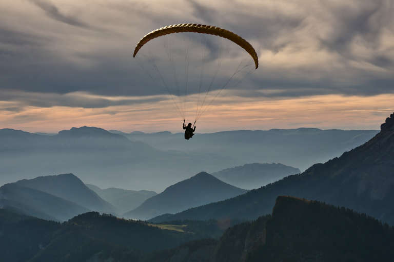 Photo de novembre en Chartreuse montrant un parapente en vol avec en arrière plan des montagnes dans la brume et des nuages texturés sur un ton orangé de couché de soleil