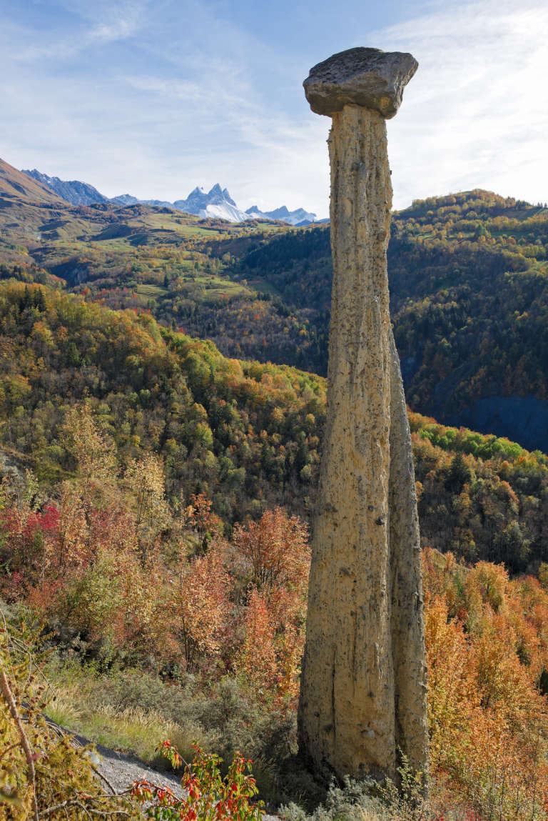 Moine de Champlan  (cheminée de roche avec un cailloux sur le dessus) devant un paysage montagneux d’automne rouge et orange