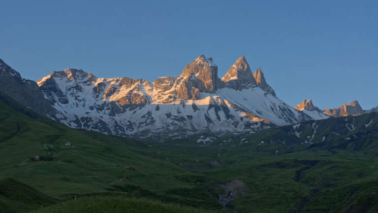 Paysage des Aiguilles d’Arves à l’aube partiellement enneigées avec au premier plan une plaine d’altitude verte à l’ombre