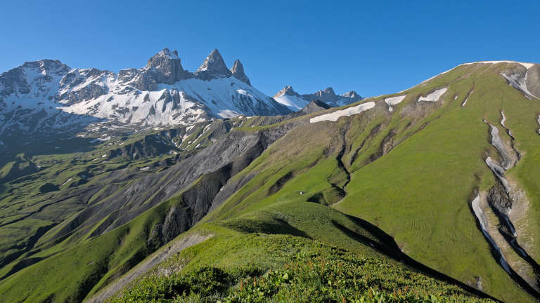 Paysage des Aiguilles d’Arves au matin avec au premier plan des reliefs de moyenne montagne verts